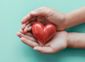 Hands holding a red stone heart.