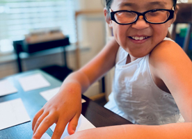 A young blind girl smiles broadly while reading a page of Braille.