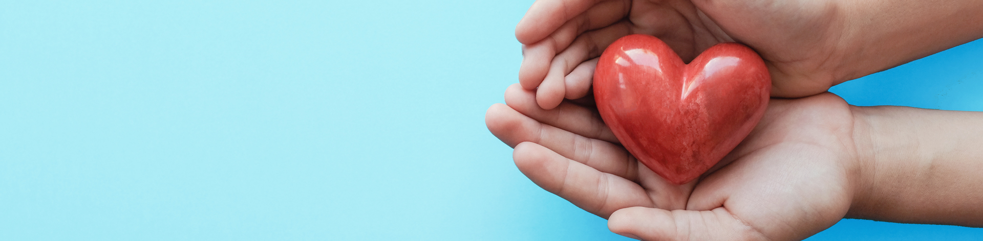 Small hands hold a red stone heart.